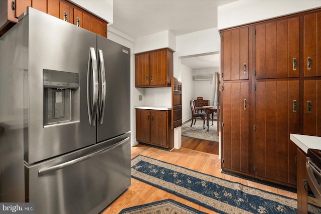 kitchen featuring light wood finished floors, brown cabinets, a wall mounted AC, stainless steel refrigerator with ice dispenser, and light countertops