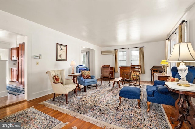 sitting room with wood finished floors, a wall unit AC, and baseboards