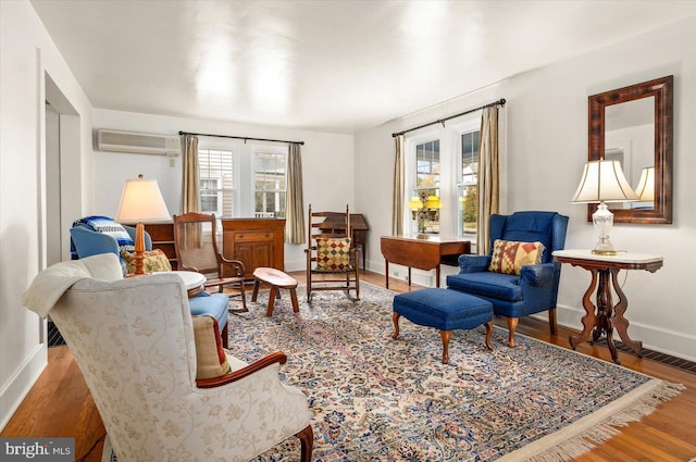 living area with visible vents, wood finished floors, a wall mounted AC, and baseboards