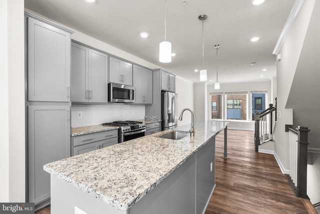 kitchen featuring dark hardwood / wood-style floors, stainless steel appliances, decorative light fixtures, and a center island with sink