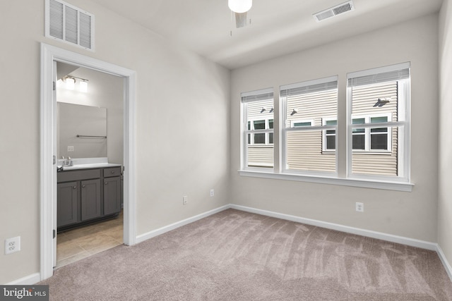 unfurnished bedroom with ensuite bath, sink, light colored carpet, and ceiling fan