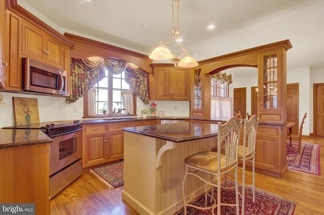 kitchen featuring a center island, stainless steel appliances, decorative light fixtures, dark stone countertops, and light hardwood / wood-style flooring