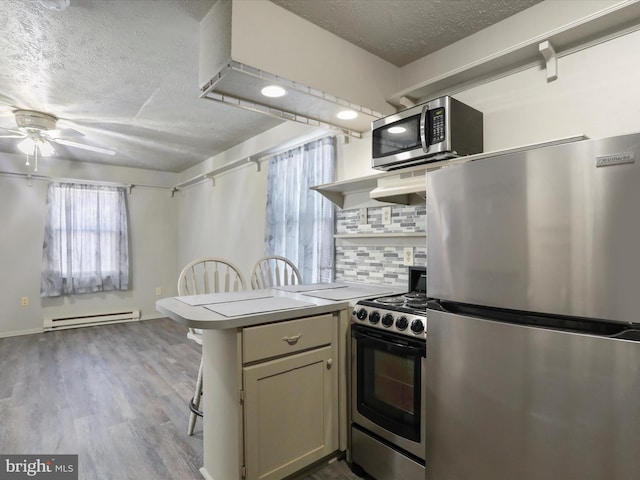 kitchen with light hardwood / wood-style flooring, kitchen peninsula, stainless steel appliances, a baseboard radiator, and a textured ceiling