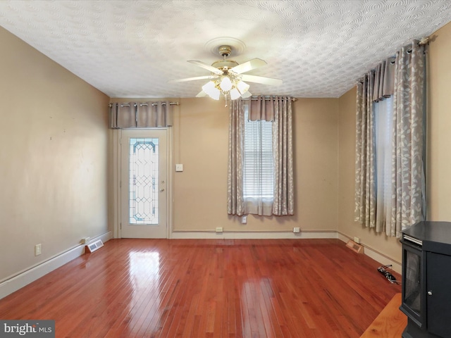 foyer entrance with a wood stove, a textured ceiling, wood-type flooring, and ceiling fan