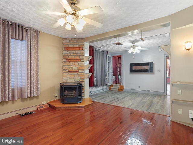 unfurnished living room featuring a wood stove, a textured ceiling, wood-type flooring, and ceiling fan