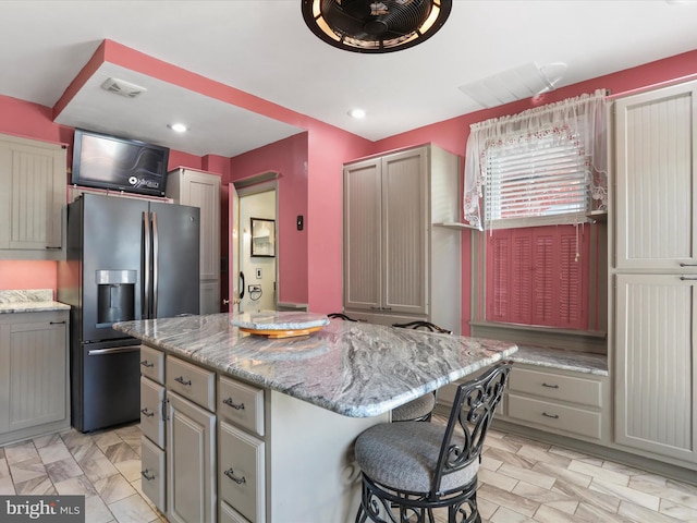 kitchen featuring light stone countertops, gray cabinetry, a kitchen island, and stainless steel fridge with ice dispenser