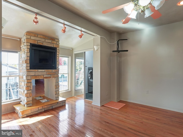 unfurnished living room with washer / dryer, a stone fireplace, hardwood / wood-style floors, ceiling fan, and vaulted ceiling