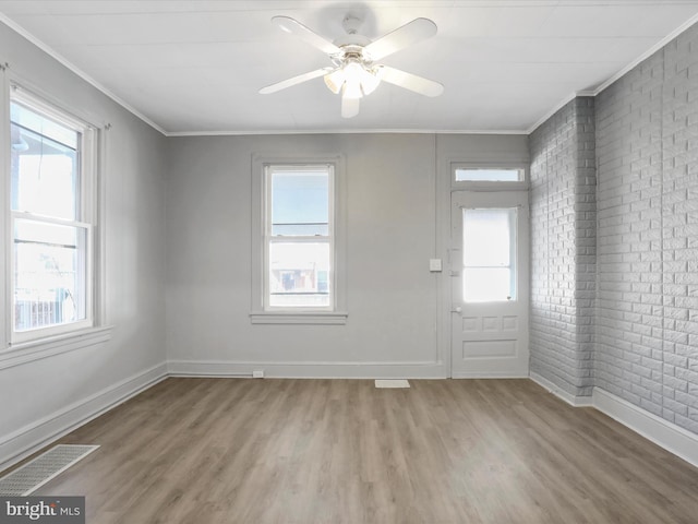 spare room with ornamental molding, hardwood / wood-style flooring, brick wall, and a wealth of natural light