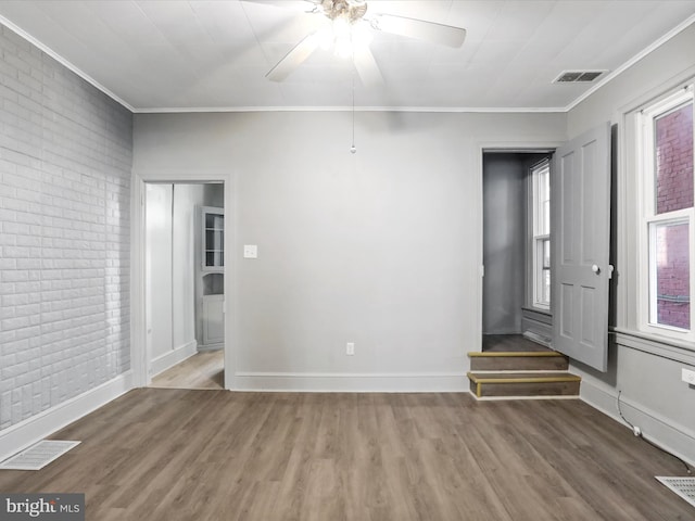 spare room with crown molding, hardwood / wood-style flooring, brick wall, and ceiling fan