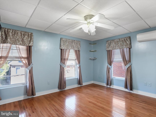 unfurnished room with a wall mounted air conditioner, wood-type flooring, and a paneled ceiling