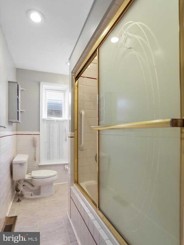 bathroom featuring tile walls, enclosed tub / shower combo, toilet, and tile patterned flooring