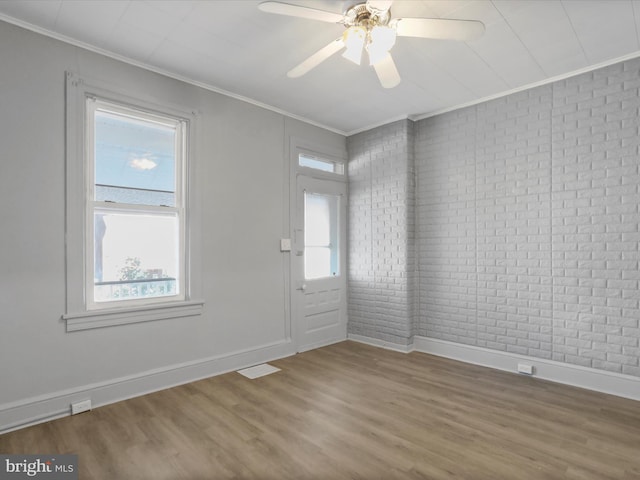 unfurnished room with hardwood / wood-style flooring, brick wall, ornamental molding, and ceiling fan