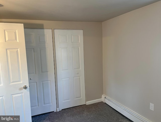 unfurnished bedroom with a baseboard heating unit and dark carpet