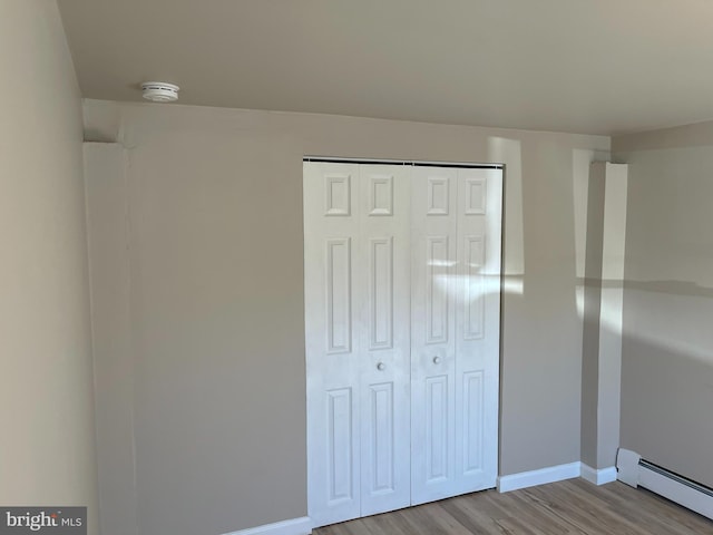 unfurnished bedroom with a closet, a baseboard heating unit, and light wood-type flooring