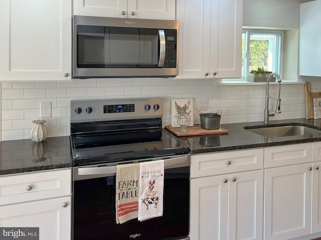 kitchen with sink, backsplash, white cabinetry, stainless steel appliances, and dark stone counters