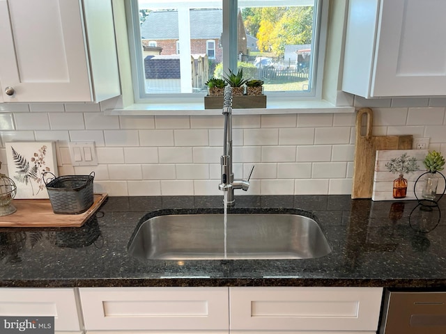 interior details featuring sink, white cabinetry, tasteful backsplash, and dark stone countertops