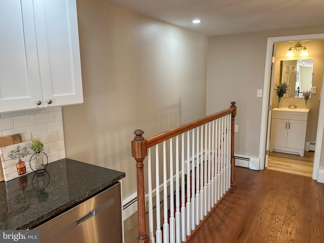 corridor with sink, a baseboard heating unit, and dark hardwood / wood-style floors