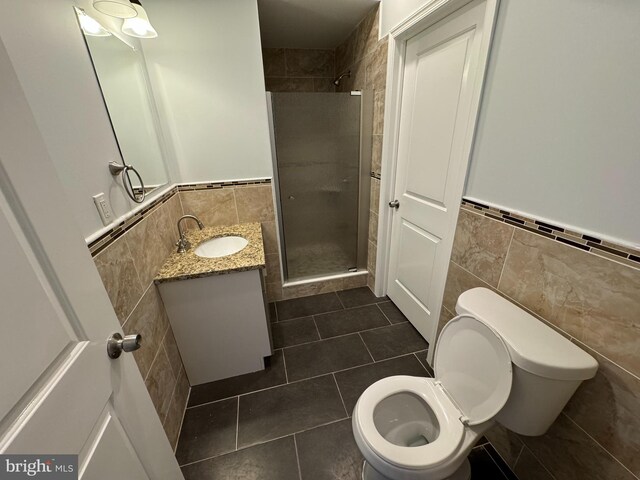 bathroom featuring vanity, toilet, tile walls, and a shower with shower door