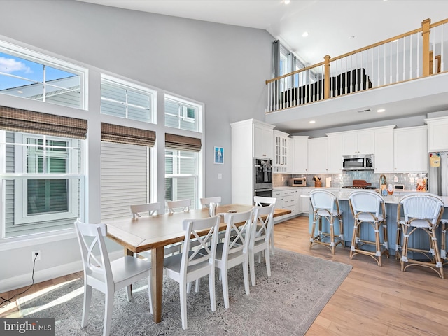 dining area featuring a healthy amount of sunlight, high vaulted ceiling, sink, and light wood-type flooring