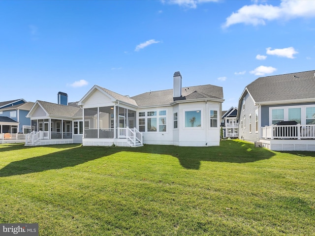 rear view of property featuring a wooden deck, a lawn, and a sunroom