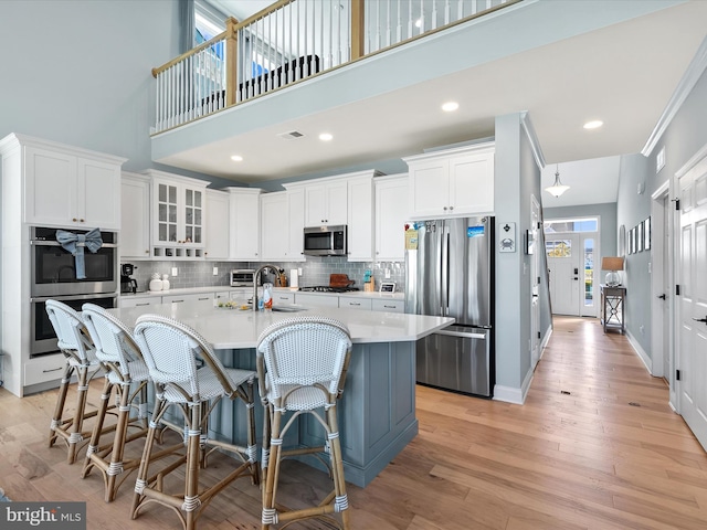 kitchen featuring appliances with stainless steel finishes, white cabinetry, a kitchen island with sink, light wood-type flooring, and sink