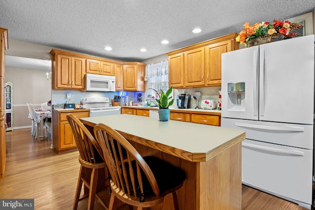 kitchen with light hardwood / wood-style floors, a center island, a kitchen bar, and white appliances