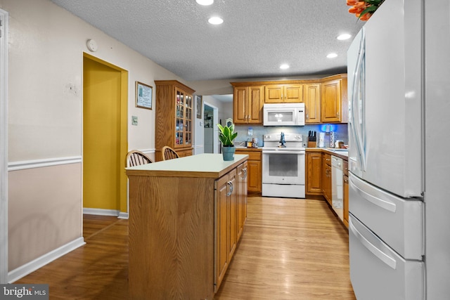 kitchen with a kitchen island, a textured ceiling, light wood-type flooring, and white appliances