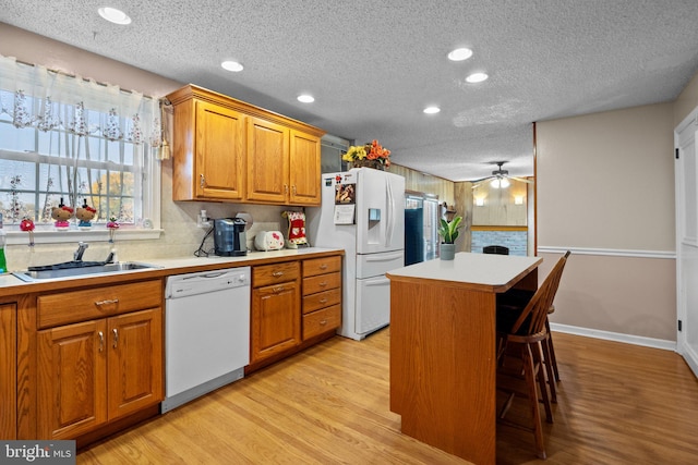 kitchen with sink, a center island, a breakfast bar, light wood-type flooring, and white appliances