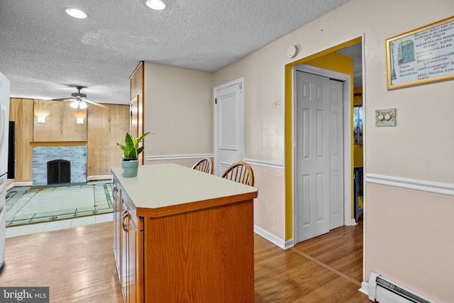 kitchen with a baseboard radiator, a stone fireplace, a textured ceiling, and light hardwood / wood-style floors