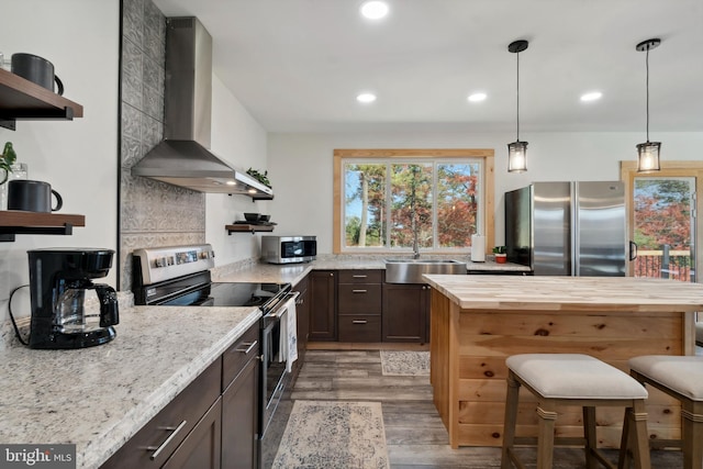 kitchen featuring light stone counters, appliances with stainless steel finishes, dark brown cabinetry, dark hardwood / wood-style flooring, and wall chimney exhaust hood