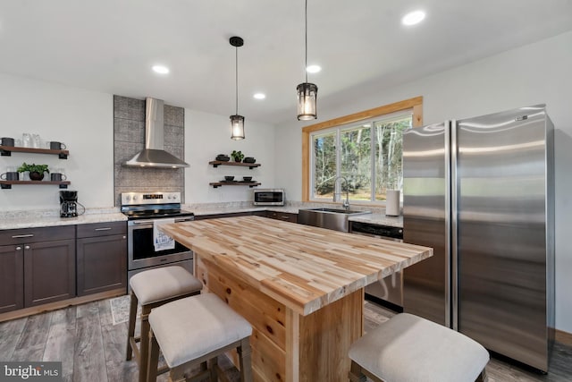 kitchen with stainless steel appliances, light wood-type flooring, decorative light fixtures, sink, and wall chimney exhaust hood