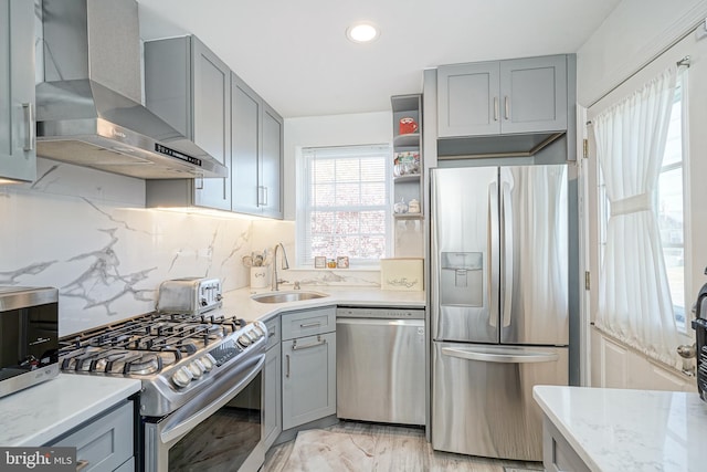 kitchen featuring stainless steel appliances, sink, light stone countertops, wall chimney range hood, and decorative backsplash