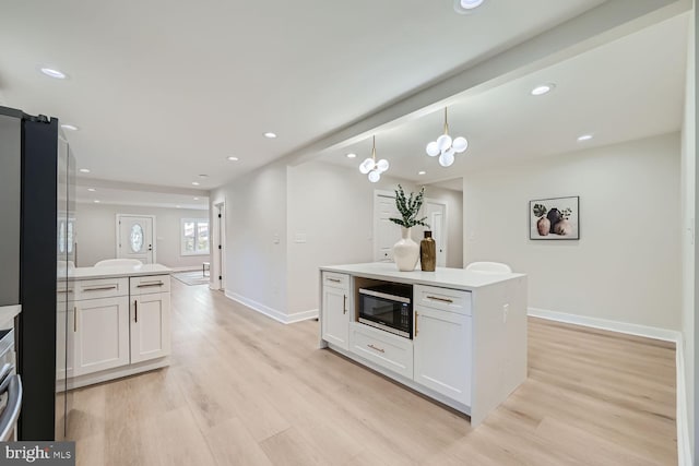 kitchen with stainless steel microwave, white cabinetry, a center island, and a chandelier