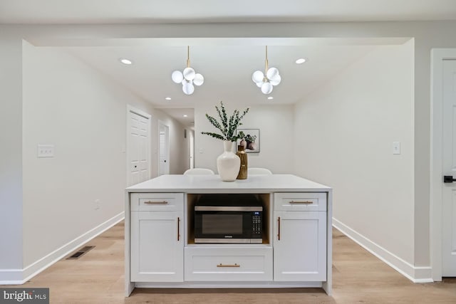 kitchen with a kitchen island, decorative light fixtures, white cabinets, a notable chandelier, and light hardwood / wood-style flooring