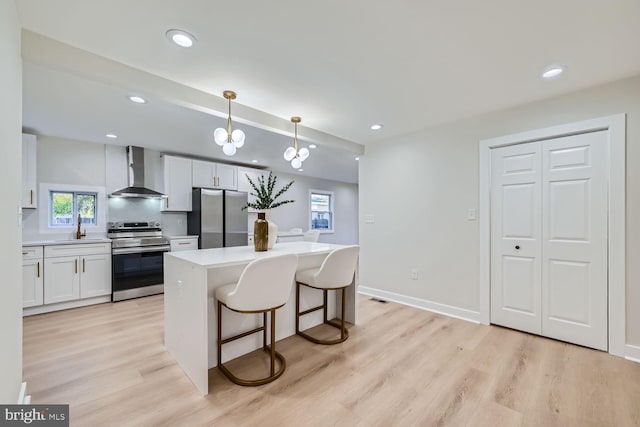 kitchen featuring wall chimney exhaust hood, appliances with stainless steel finishes, hanging light fixtures, and white cabinets