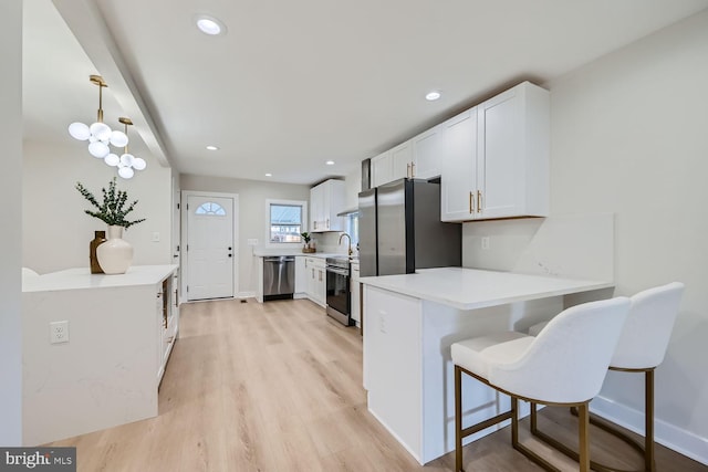 kitchen featuring kitchen peninsula, white cabinets, appliances with stainless steel finishes, pendant lighting, and light hardwood / wood-style floors