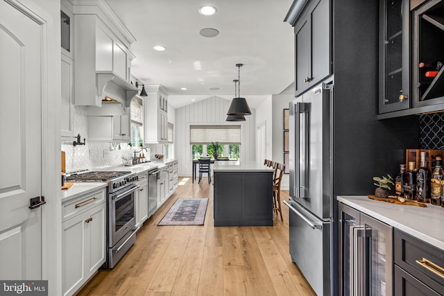 kitchen featuring premium appliances, tasteful backsplash, hanging light fixtures, white cabinetry, and light hardwood / wood-style floors