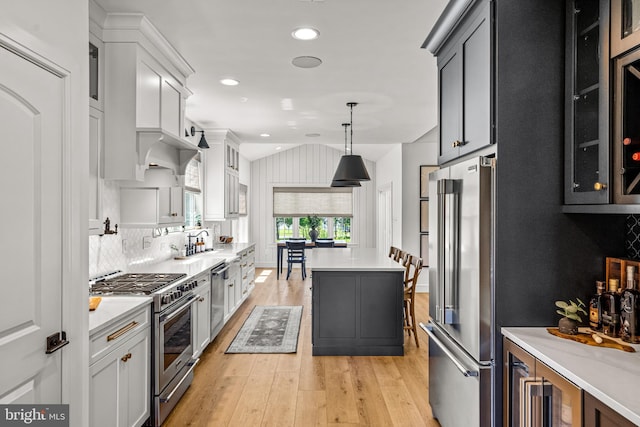 kitchen with tasteful backsplash, light wood-type flooring, a center island, hanging light fixtures, and high end appliances