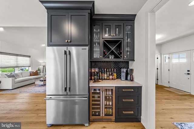 bar with light hardwood / wood-style flooring, decorative backsplash, beverage cooler, and high end refrigerator