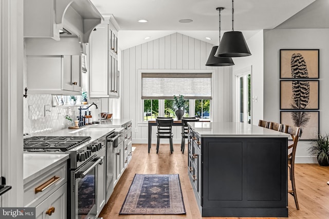 kitchen featuring appliances with stainless steel finishes, a center island, hanging light fixtures, white cabinetry, and light hardwood / wood-style floors