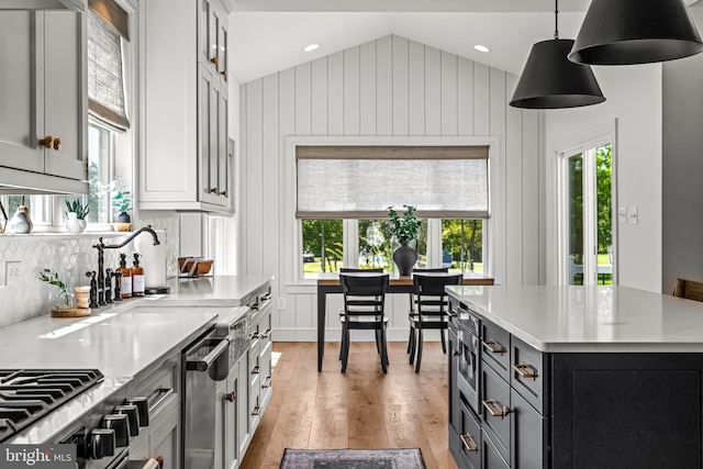 kitchen featuring hanging light fixtures, backsplash, vaulted ceiling, a center island, and light hardwood / wood-style floors