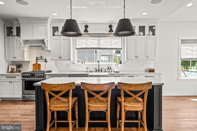 kitchen with high end stove, backsplash, white cabinetry, and light hardwood / wood-style floors