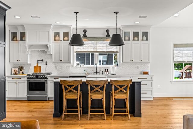 kitchen with tasteful backsplash, high end stainless steel range oven, decorative light fixtures, white cabinets, and light hardwood / wood-style flooring