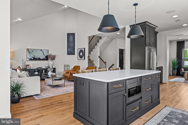 kitchen with light wood-type flooring, a kitchen island, stainless steel appliances, decorative light fixtures, and gray cabinets