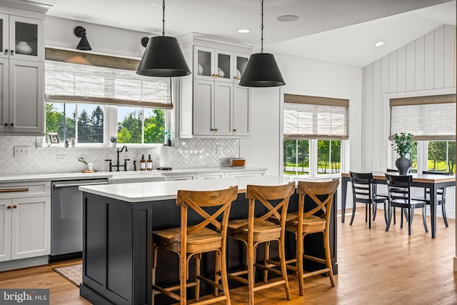 kitchen featuring stainless steel dishwasher, a center island, hanging light fixtures, and light hardwood / wood-style floors