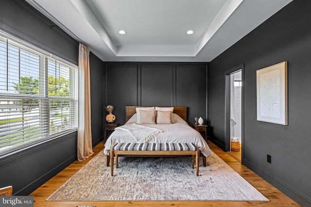 bedroom with light wood-type flooring and a raised ceiling