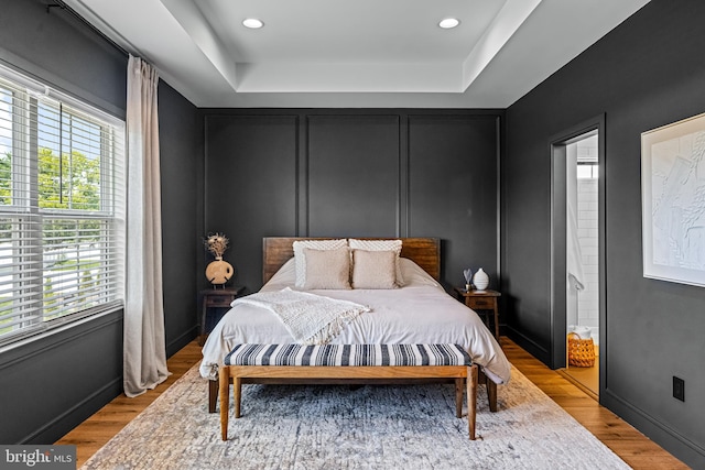 bedroom with light hardwood / wood-style flooring, multiple windows, and a tray ceiling