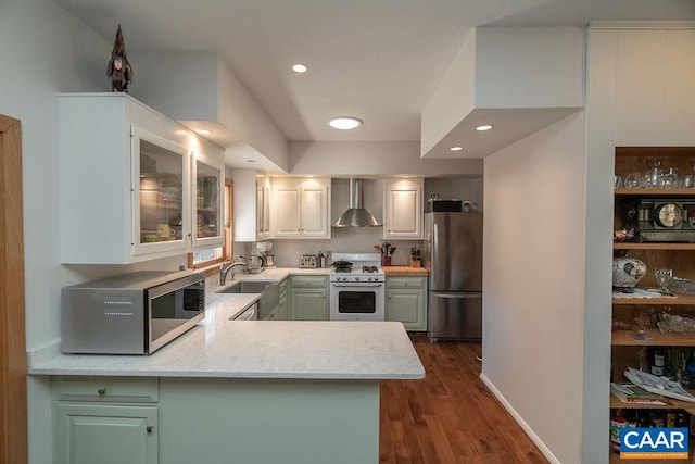 kitchen with wall chimney range hood, dark wood-type flooring, kitchen peninsula, stainless steel appliances, and white cabinetry