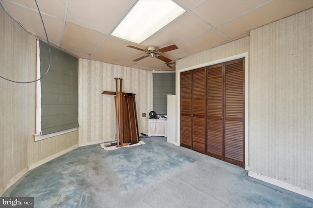 unfurnished bedroom featuring a drop ceiling, carpet floors, a closet, and ceiling fan