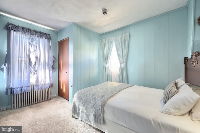 carpeted bedroom featuring multiple windows, wooden walls, and radiator